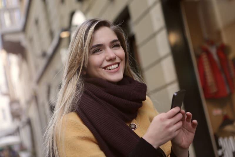 Eine lächelnde Frau steht mit einem Smartphone in der Hand auf der Straße