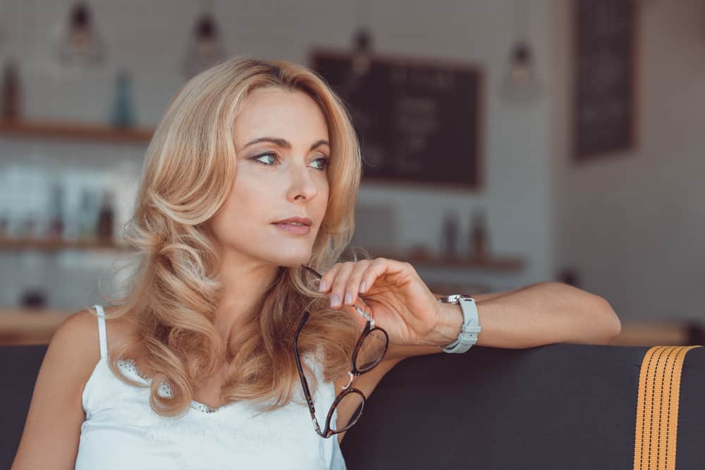 Eine schöne Blondine sitzt mit einer Brille in der Hand auf der Couch und denkt nach
