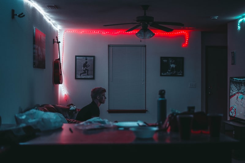Mann sitzt im Zimmer in der Nähe von Jalousien mit eingeschalteten Lichtern