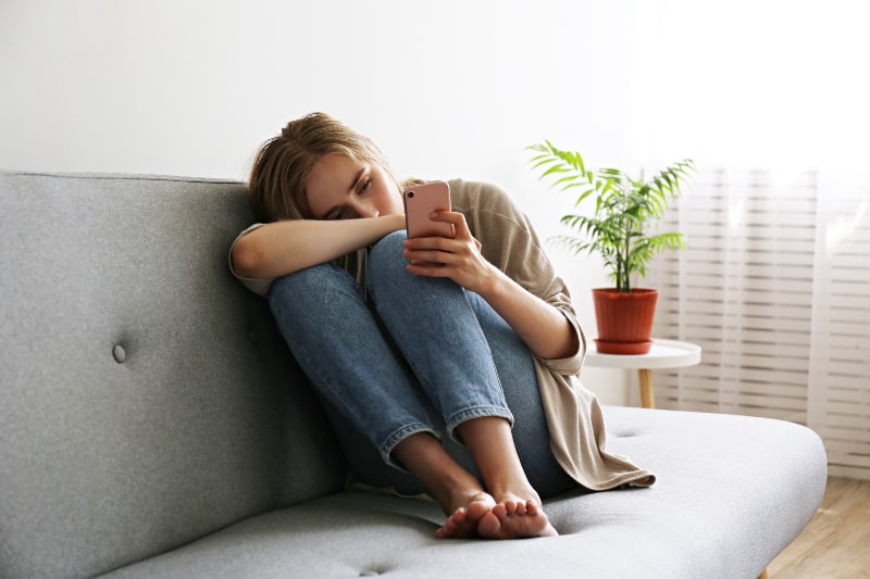 depressives Mädchen sitzt auf der Couch und schaut auf Handy