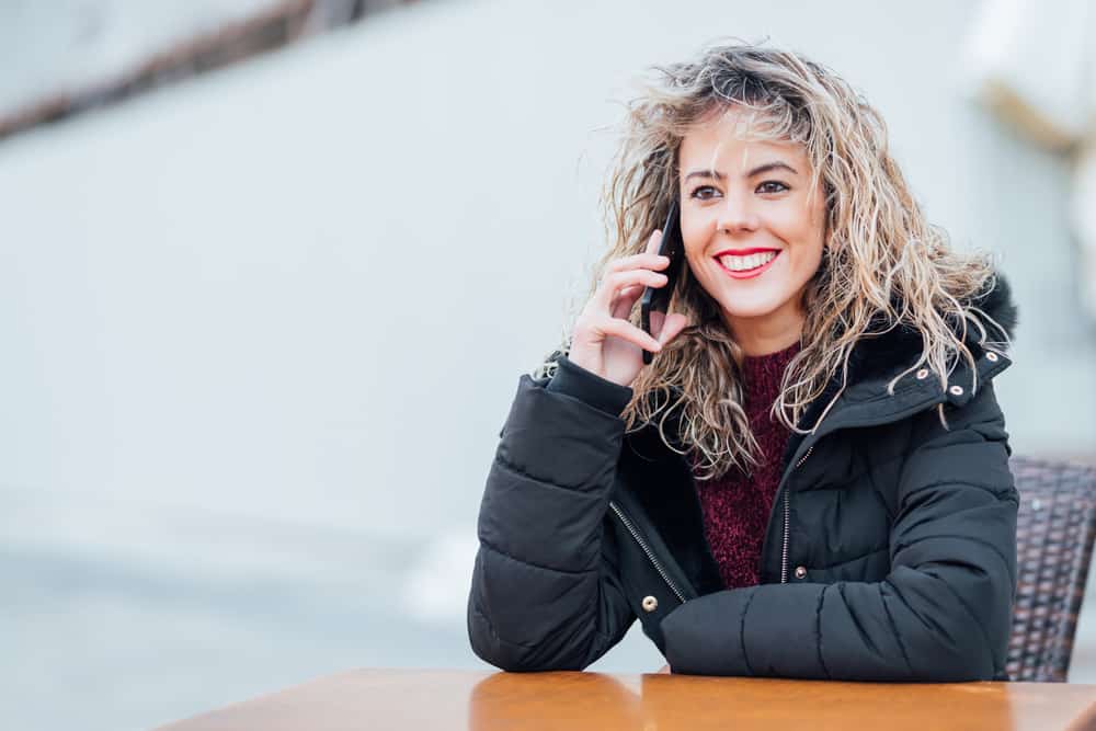 glückliche Frau in der Winterjacke, die am Handy sitzt und spricht