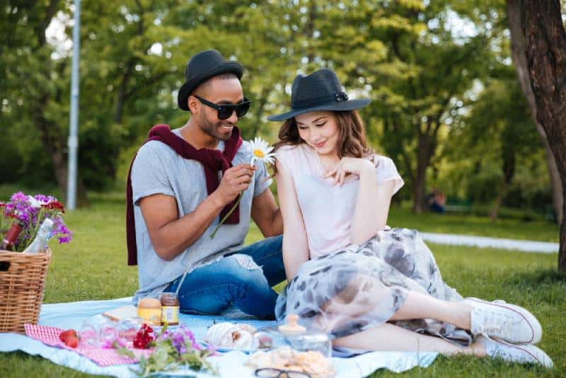 lächelnder junger Mann, der seiner schüchternen Freundin beim Picknick Blume gibt