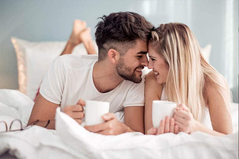 lächelndes Paar, das auf Bett liegt und Tasse Tee hält