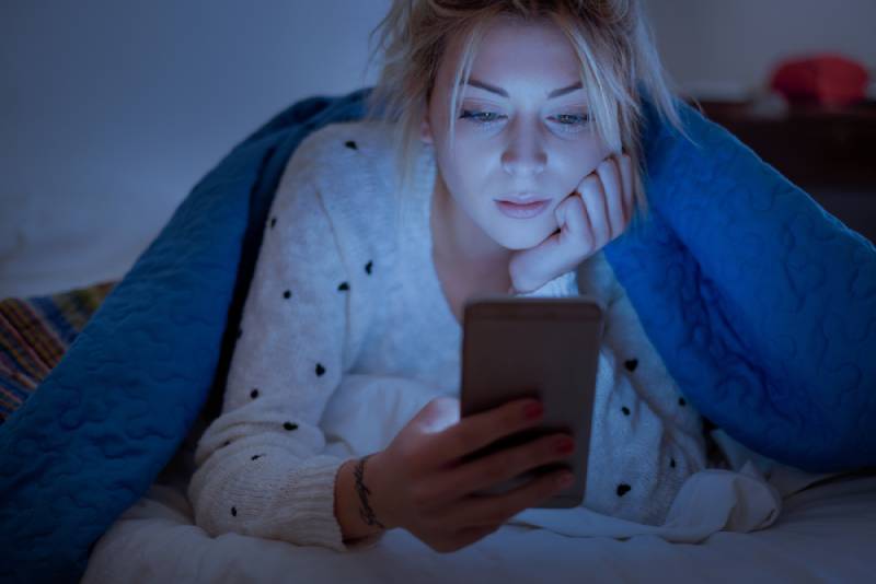 traurige Frau, die ihr Telefon während der Nacht benutzt, während sie auf dem Bett liegt