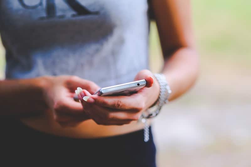 weibliche Hände mit weißem Nagellack, der ein Smartphone hält