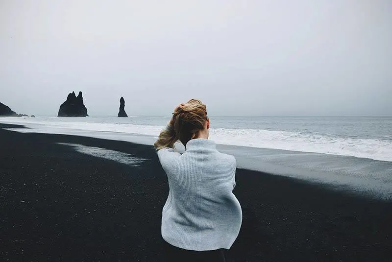 eine Frau in einem Pullover, die am Strand steht und ihren Kopf hält