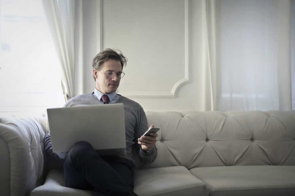 Ein Geschäftsmann auf der Couch mit einem Laptop und einem Handy in der Hand
