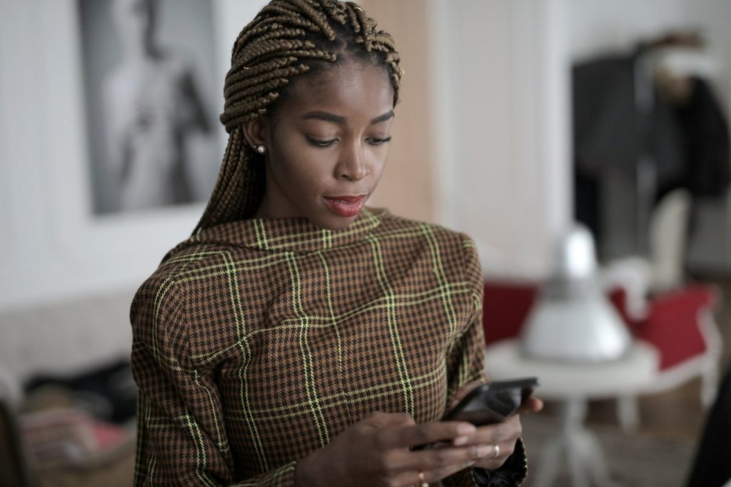 Eine schwarze Frau mit Dreadlocks schreibt etwas auf ihr Handy