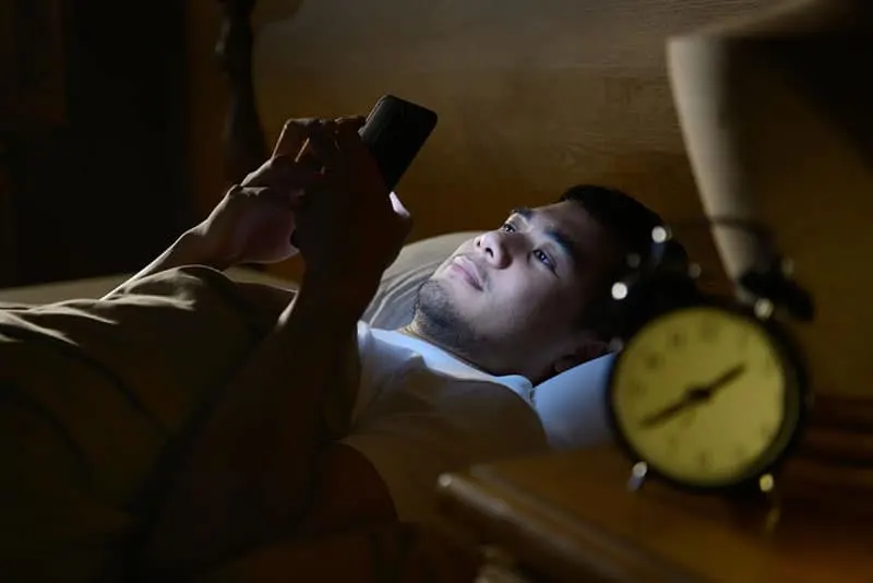 Mann auf dem Bett liegen und auf seinem Telefon tippen