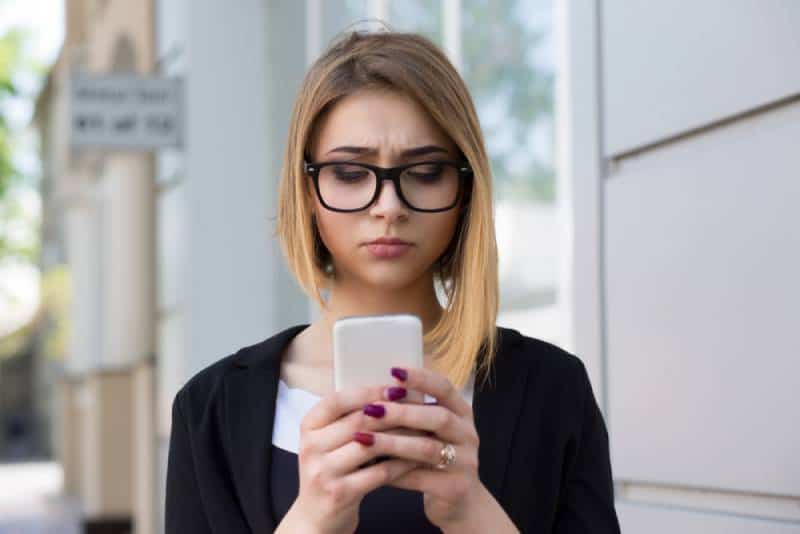 unglückliches Mädchen, das draußen auf ihr Telefon schaut