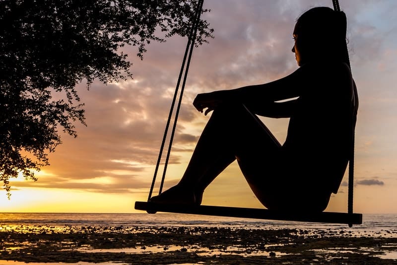 Das Mädchen sitzt auf einer Schaukel und beobachtet den Sonnenuntergang