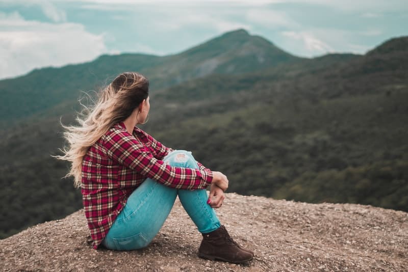 Ein Mädchen in einem karierten Hemd sitzt auf einem Felsen und beobachtet die Landschaft
