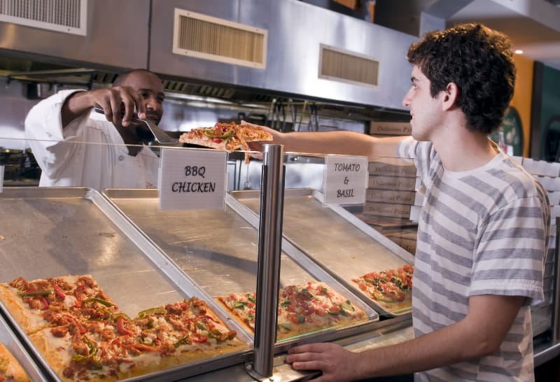 Ein junger Mann kauft ein Stück Pizza in einem Restaurant
