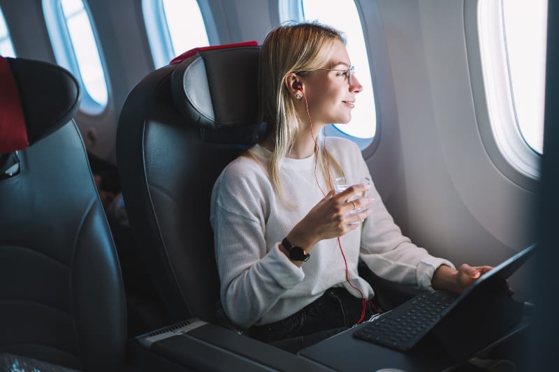 Ein junges Mädchen in einem Flugzeug mit einem Laptop in den Händen schaut aus dem Fenster