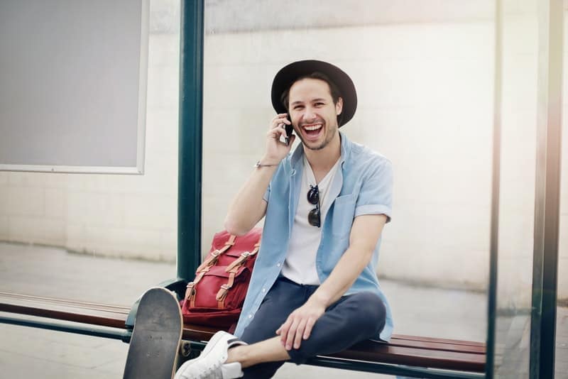 Ein lächelnder Mann mit Schlittschuh und Rucksack spricht auf seinem Handy
