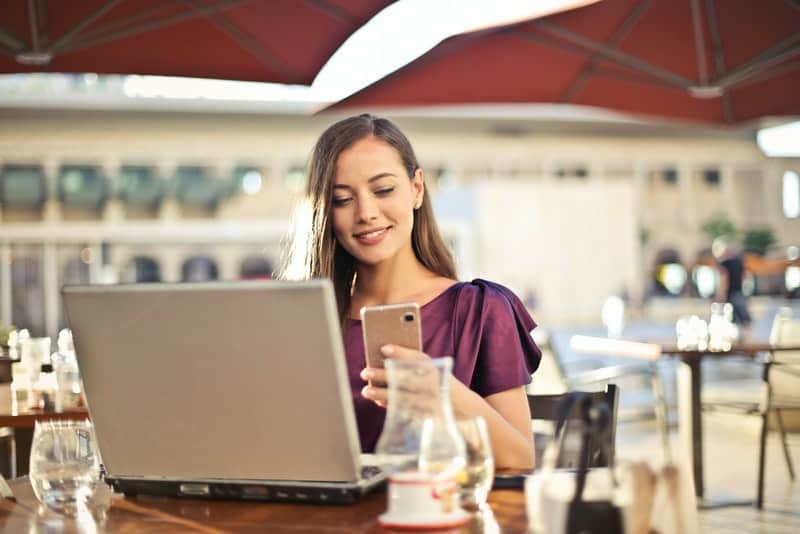 Eine Frau sitzt auf einer Kaffeeterrasse und liest glücklich eine SMS