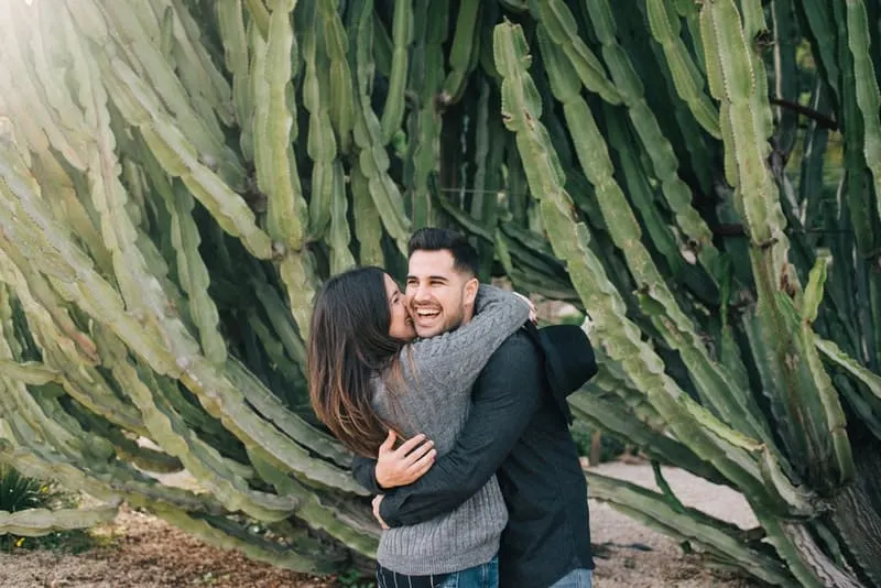 Eine Frau umarmt einen lächelnden Mann neben einem Kaktus