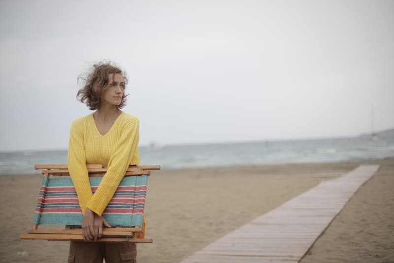 Eine traurige Frau hält eine Liege in den Händen und geht zum Strand