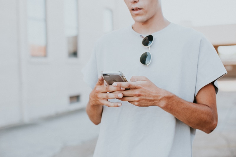 Mann im weißen Top mit Rundhalsausschnitt und Smartphone im Freien(1)
