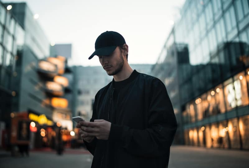 Mann in schwarzer Jacke mit schwarzer Mütze beim Telefonieren