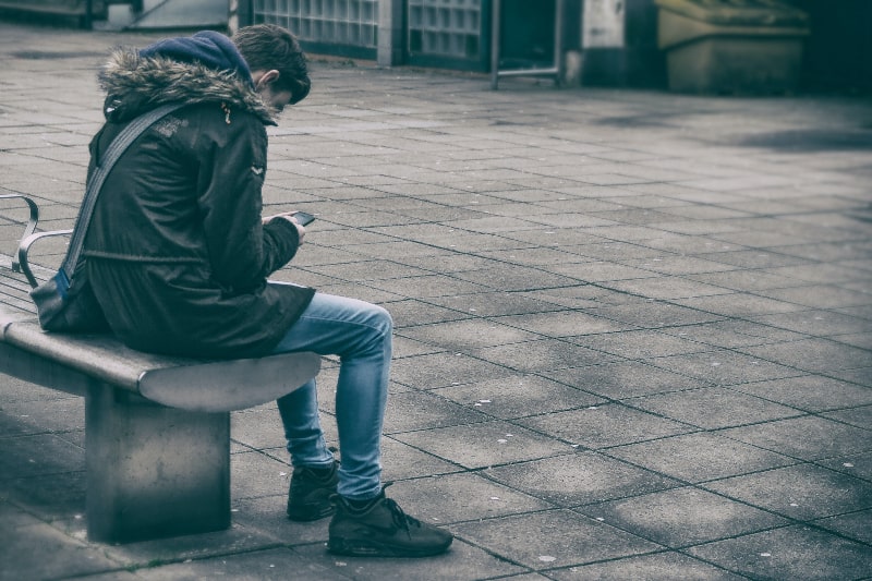 Mann sitzt auf Bank, die Telefon hält