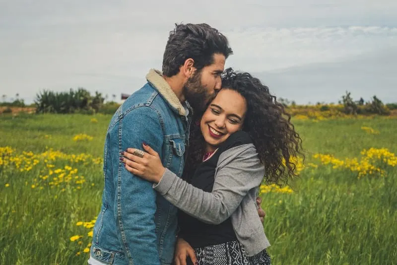 Ein Mann mit Bart auf einem Grasfeld küsst ein lächelndes Mädchen auf die Wange