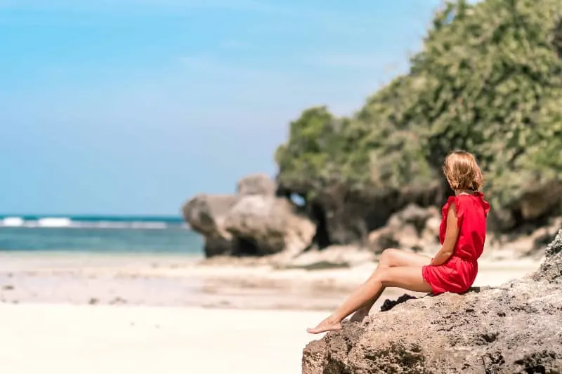 ein Mädchen beobachtet den Strand und sitzt auf einem Felsen(1)