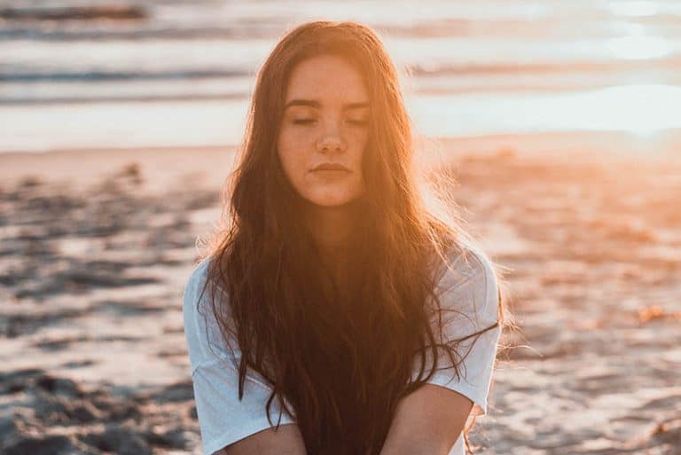 Ein junges Mädchen mit langen Haaren meditiert am Strand