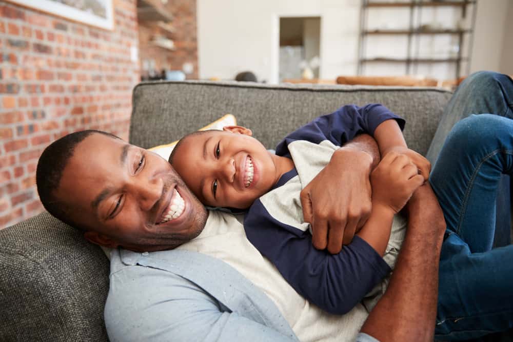 Ein lächelnder Vater und ein lächelnder Sohn liegen in einer Umarmung auf der Couch
