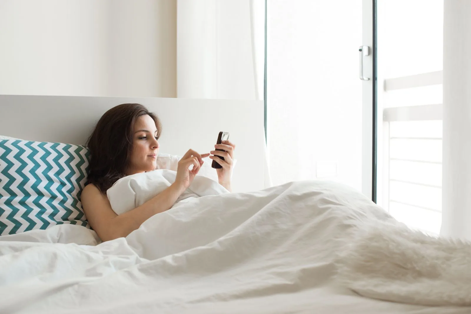 Eine Frau liegt mit einem Telefon im Bett