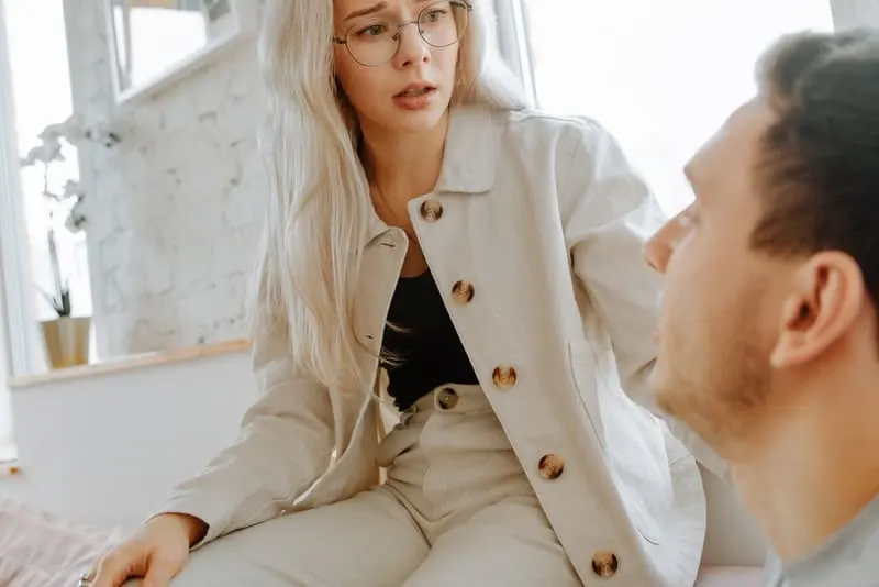 Eine besorgte Frau mit Brille sitzt auf der Couch und spricht mit ihrem Mann