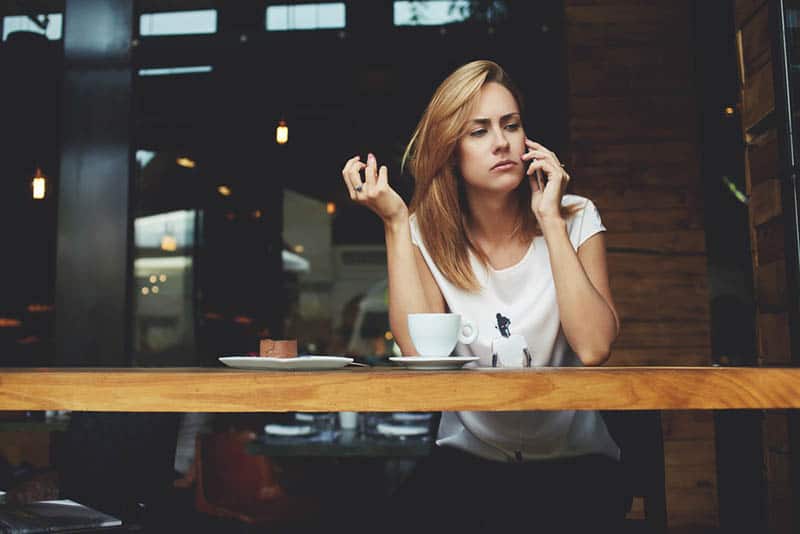 Frau sieht nachdenklich aus, während sie im Café telefoniert