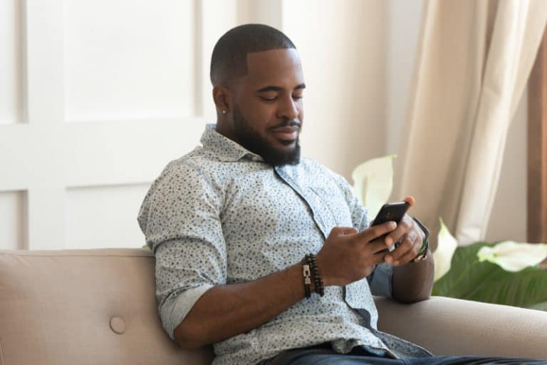 Glücklicher positiver nachdenklicher Afroamerikaner, der auf Sofa sitzt