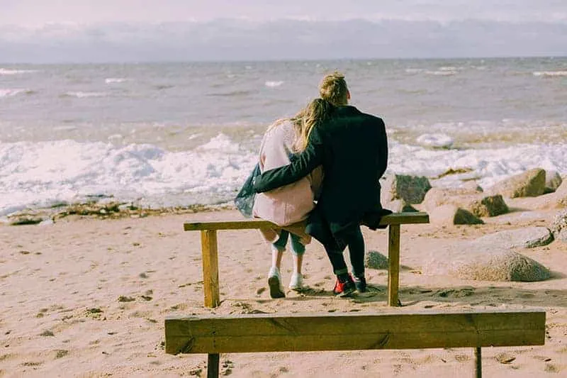Mann, der Frau beim Sitzen am Strand umarmt