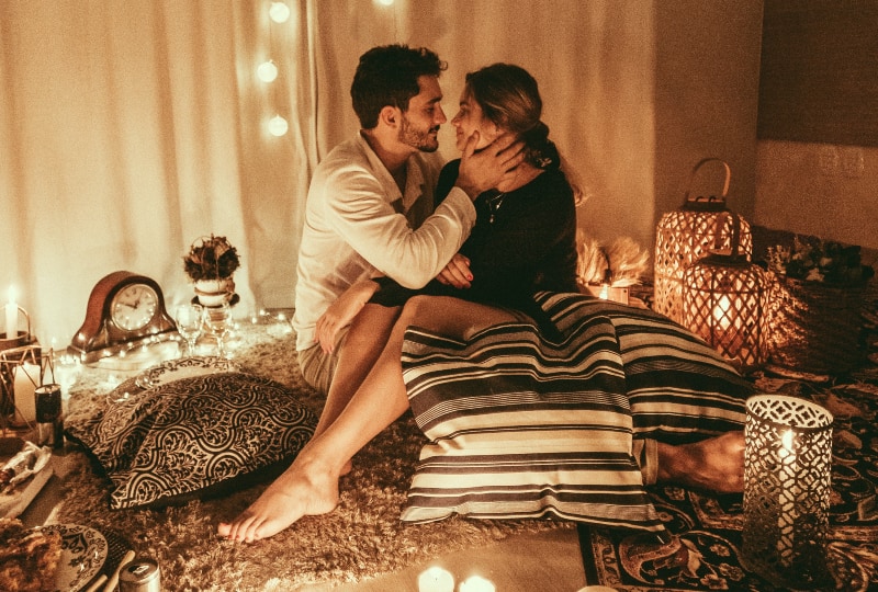Mann und Frau sitzen auf dem Boden und küssen sich mit brennenden Kerzen im Zimmer