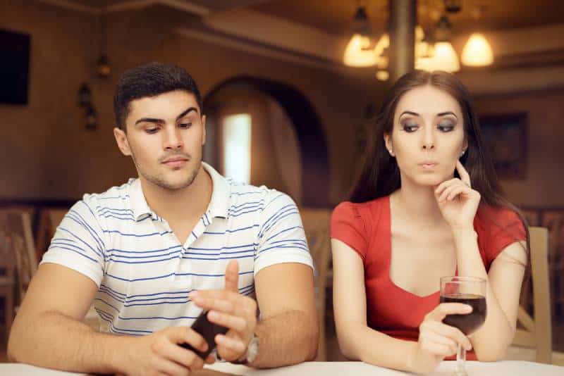 Neugieriges Mädchen, das Freund auf Smartphone ausspioniert