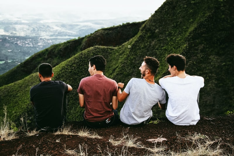 Reihe von vier Männern, die auf Bergpfad sitzen