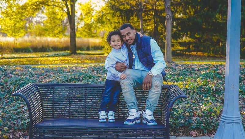 ein lächelnder Vater mit einem Kind, das auf einer Parkbank sitzt