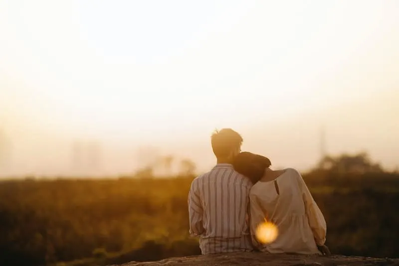 ein trauriges Paar, das auf einem Felsen sitzt und den Sonnenuntergang beobachtet