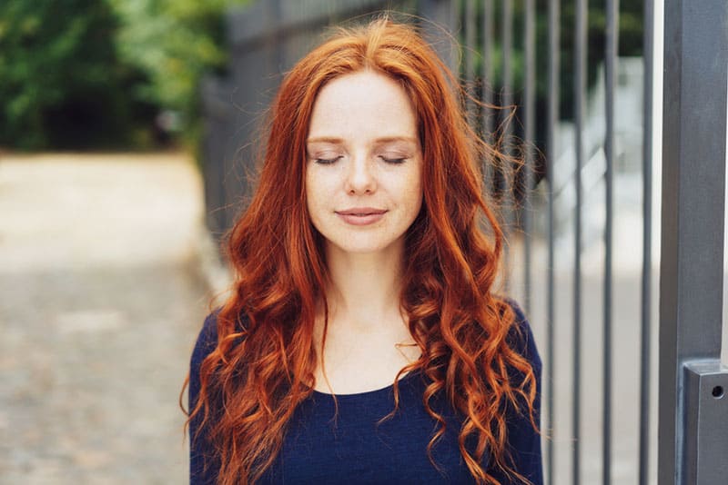 junge Frau mit roten Haaren, die geschlossene Augen halten