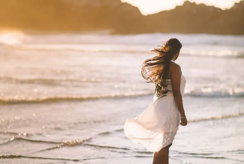 ein Mädchen in einem weißen Kleid, das alleine am Meer spazieren geht