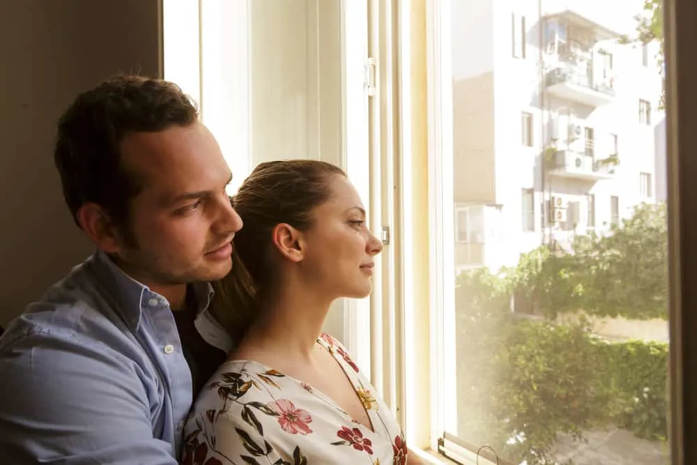 Ein liebevolles Paar in einer Umarmung steht auf und schaut aus dem Fenster