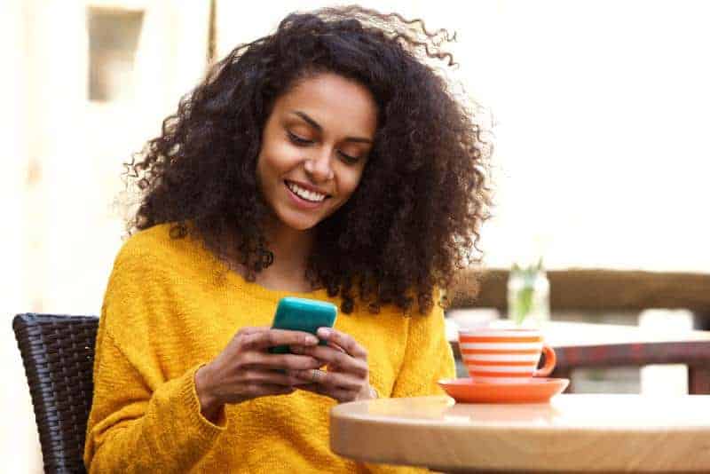 Frau, die im Café sitzt und auf ihrem Telefon tippt