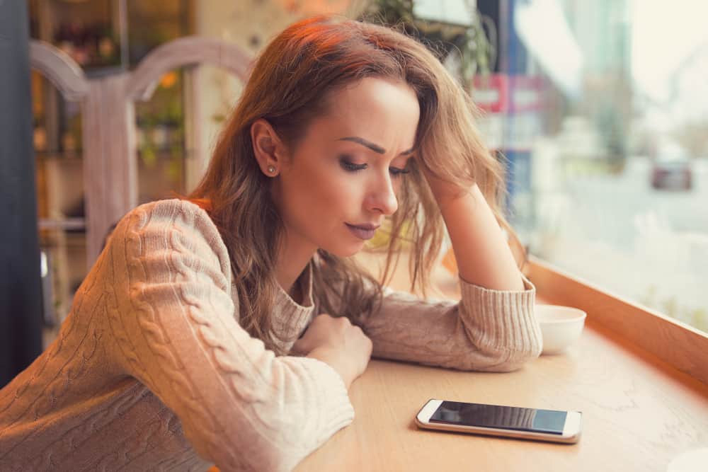eine Frau, die in einem Café sitzt und traurig auf ihr Handy schaut