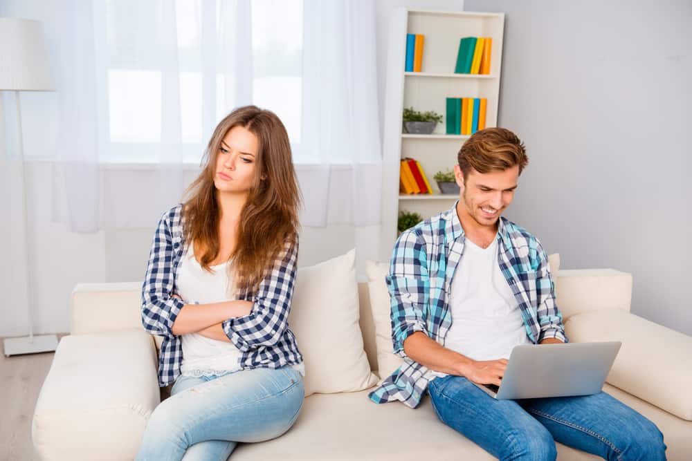 eine traurige Frau, die auf der Couch neben einem lächelnden Mann sitzt, der einen Laptop benutzt