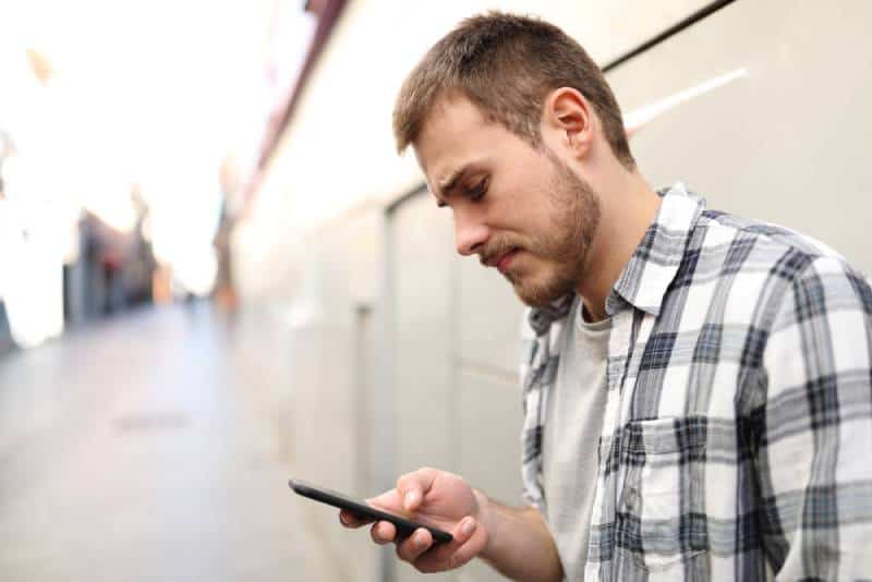 unglücklicher Mann, der auf seinem Telefon eine SMS schreibt