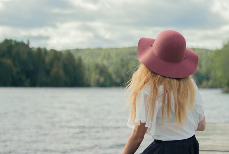 Ein Mädchen mit Hut sitzt am See