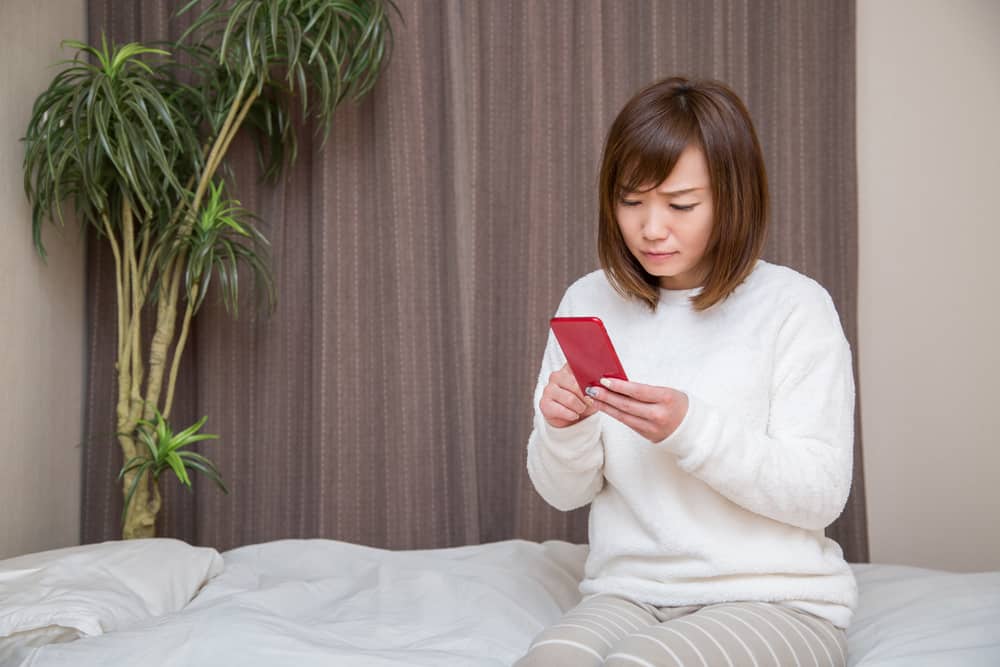 Eine besorgte Frau im Schlafzimmer benutzt ein Handy