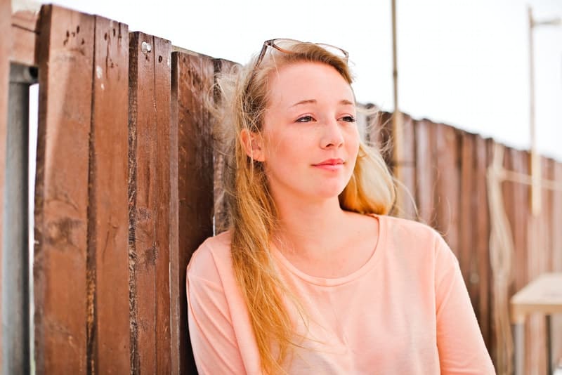 Eine schöne Blondine steht an einem Holzzaun gelehnt