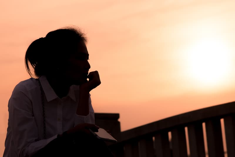 Eine traurige Frau sitzt allein während des Sonnenuntergangs
